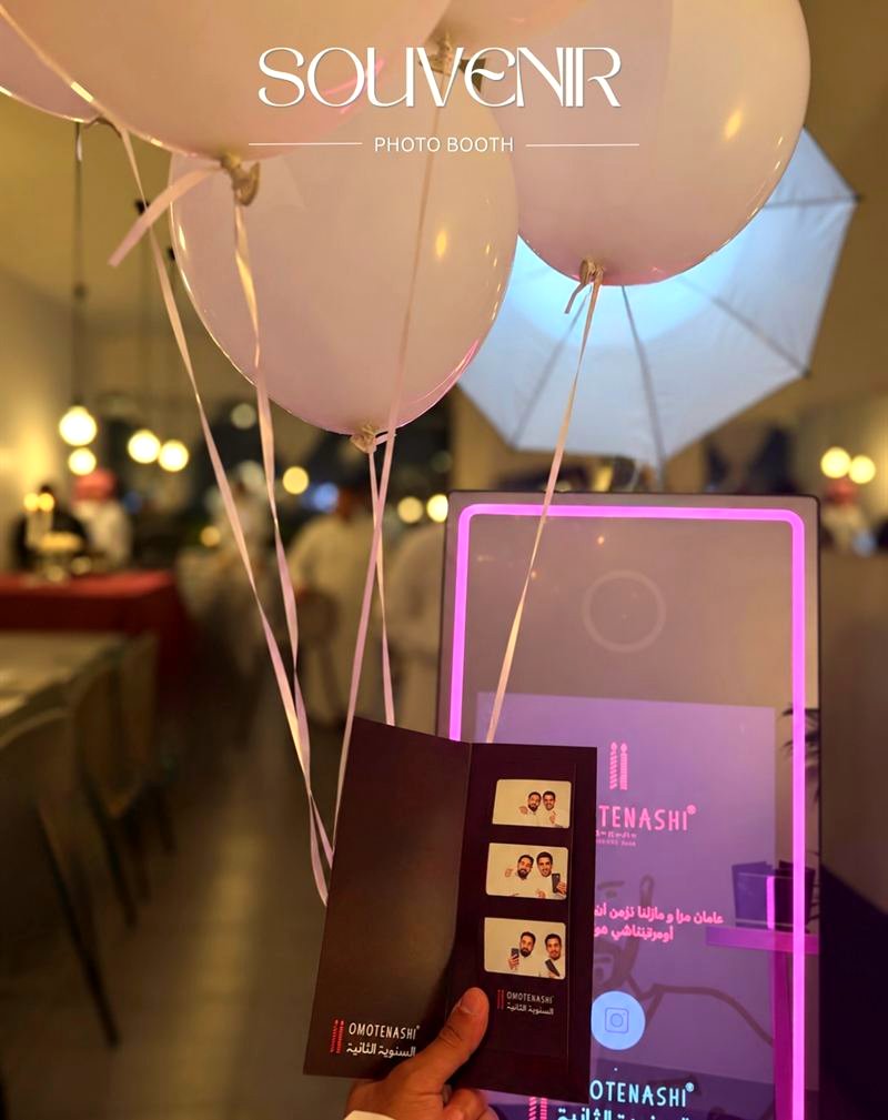 Guest holding a printed photo strip beside the pink-lit booth and balloons